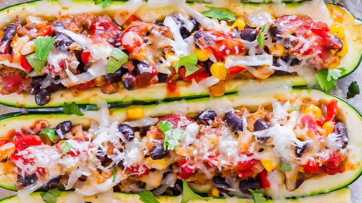 Two zucchini boats filled with a colorful mixture of diced tomatoes, black beans, corn, melted cheese, and garnished with chopped cilantro. The dish is vibrant and garnished, showcasing a hearty and healthy meal option.